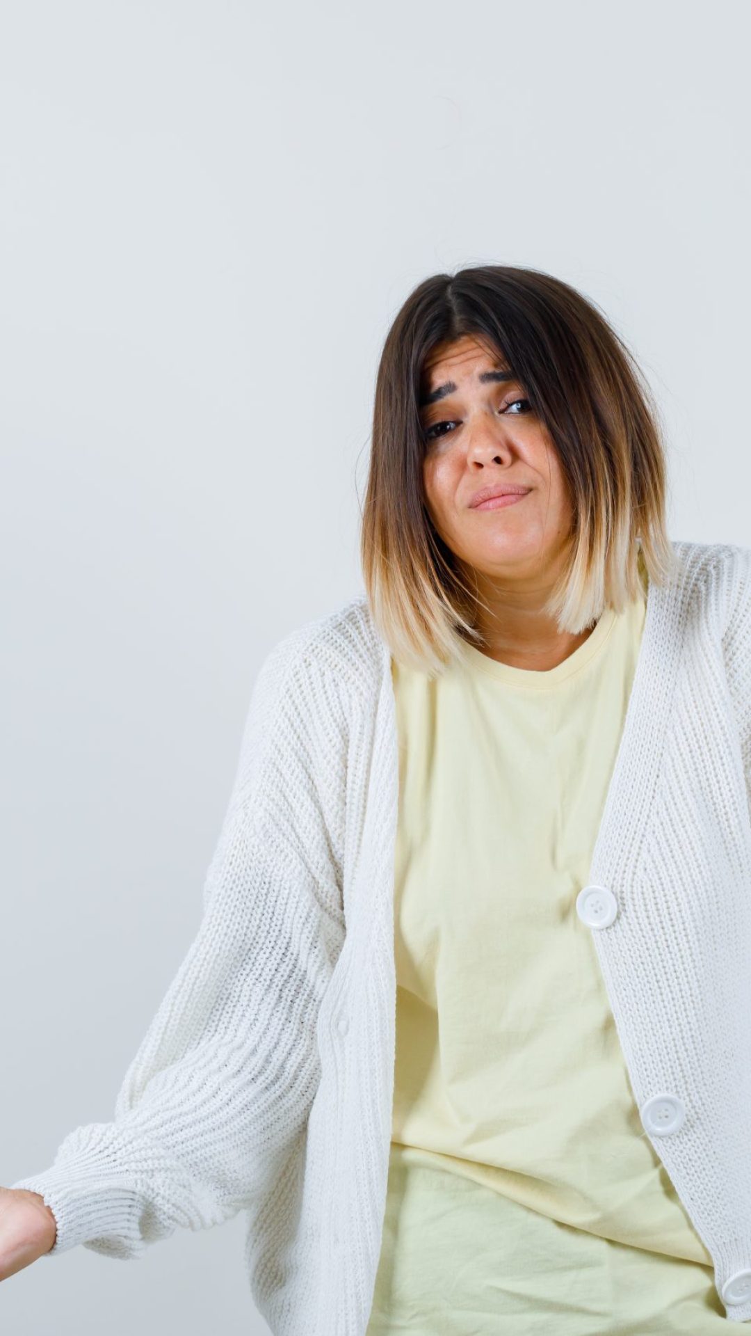 young girl showing helpless gesture in yellow t-shirt, white cardigan and looking worried. front view.